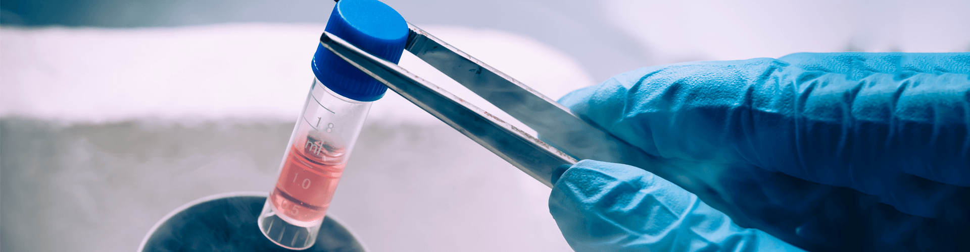 Gloved hand holds test tube with red liquid using metal tongs; numbers 18 and 10 visible.