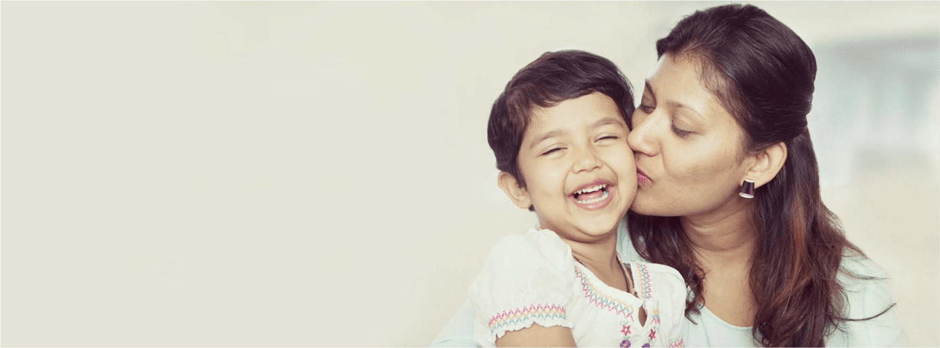 Woman kissing happy child on the cheek in soft light, showing warmth and emotional bonding.