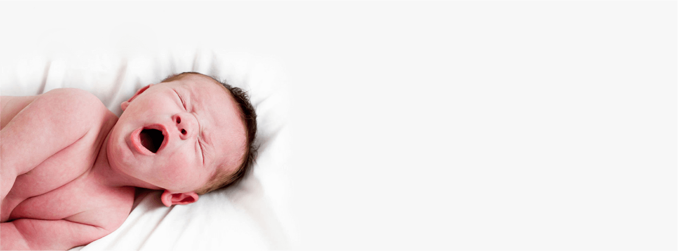 Baby yawns while lying on soft white surface; peaceful and serene newborn moment.