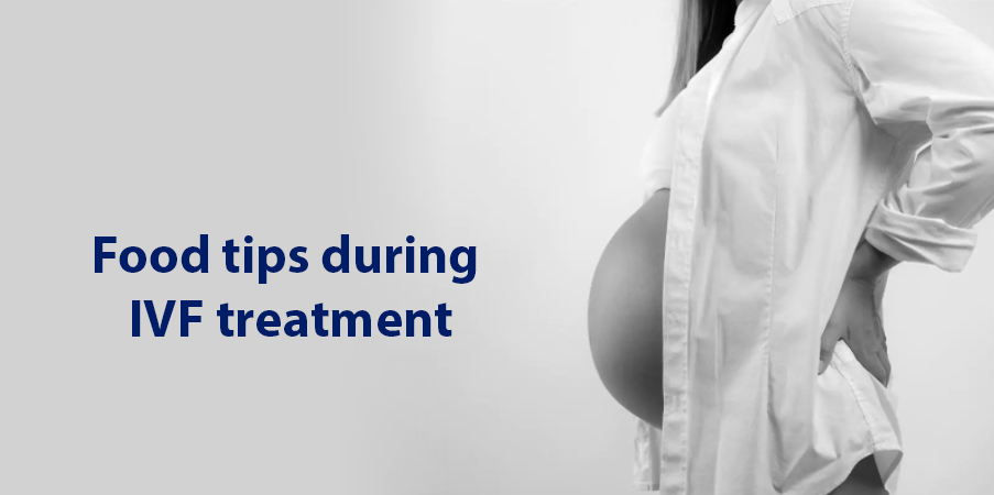 Pregnant person in white shirt with hands on hips; plain background with overlay: “Food tips during IVF treatment.”