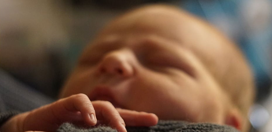 Sleeping newborn’s tiny hand rests on blanket; blurred background adds intimacy and calm.