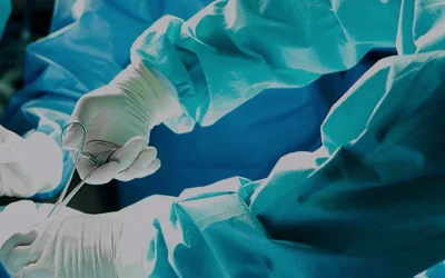 Surgical team operates in sterile room with precise tool use; focused hands in blue gowns.